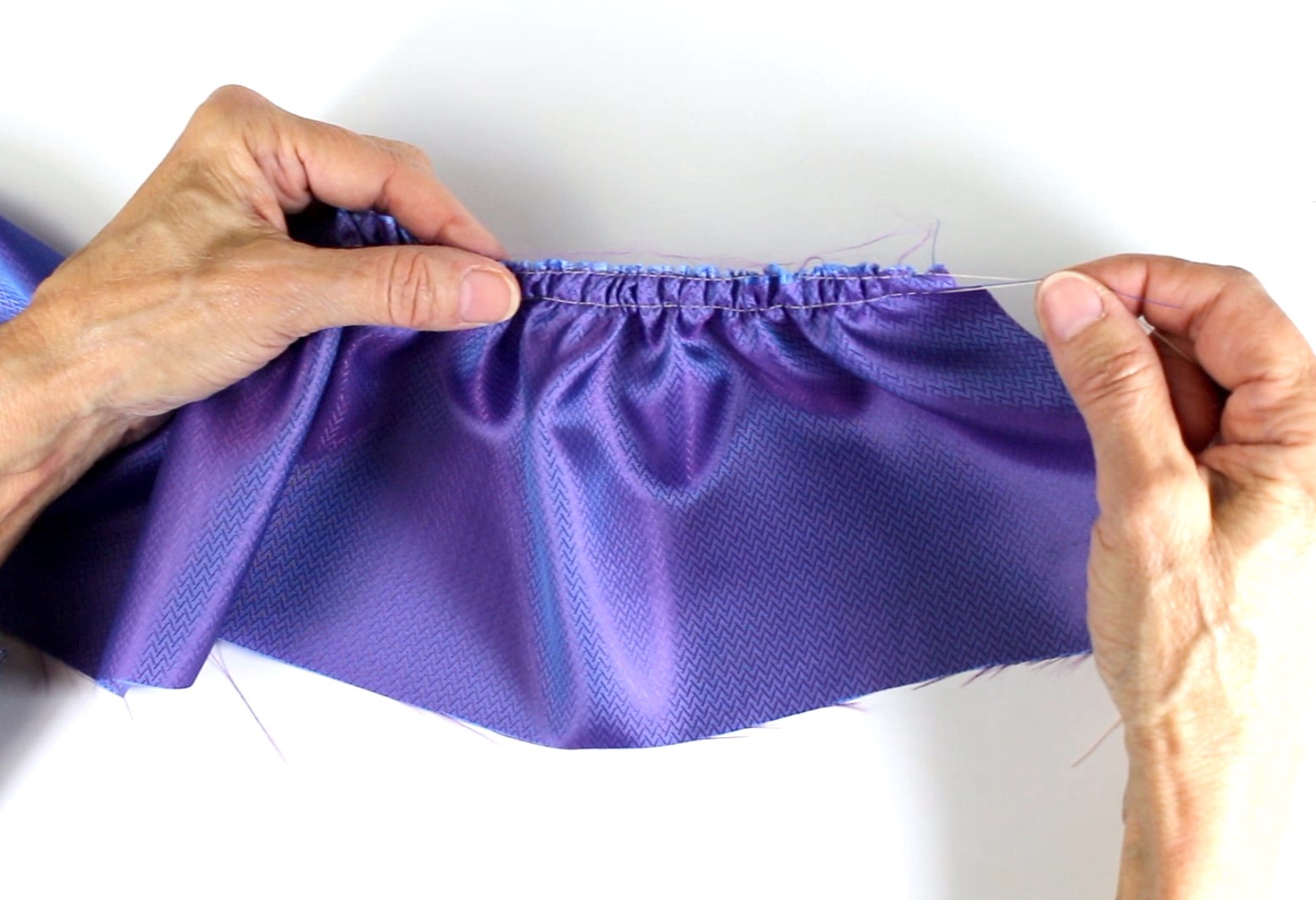 Selbstgemachte Naht mit gerafftem, lila Stoff. Modisches Handarbeiten, ideal für kreative Nähprojekte.