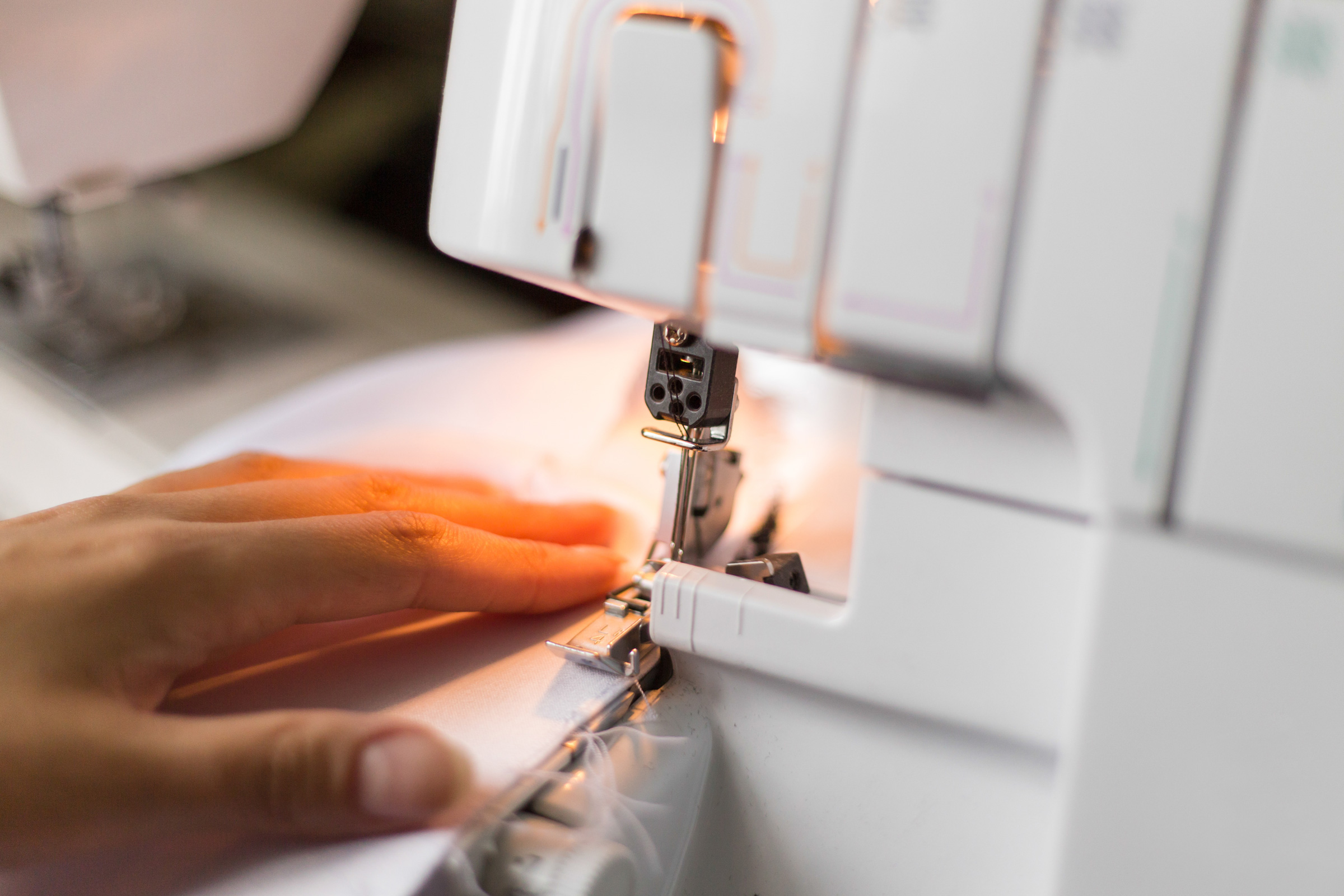Nähen: Präzision, DIY, kreative Handarbeit. Weißes, schlichtes Material unter der Maschine.