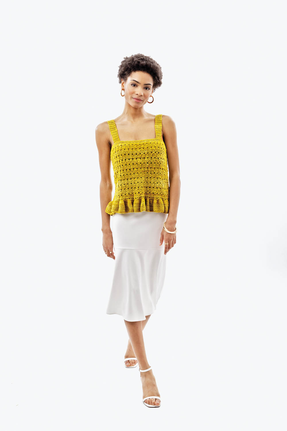 Modisch gehäkeltes Top in Senfgelb, strukturierte Muster, voluminöser Saum. Schlichter weißer Midi-Rock.