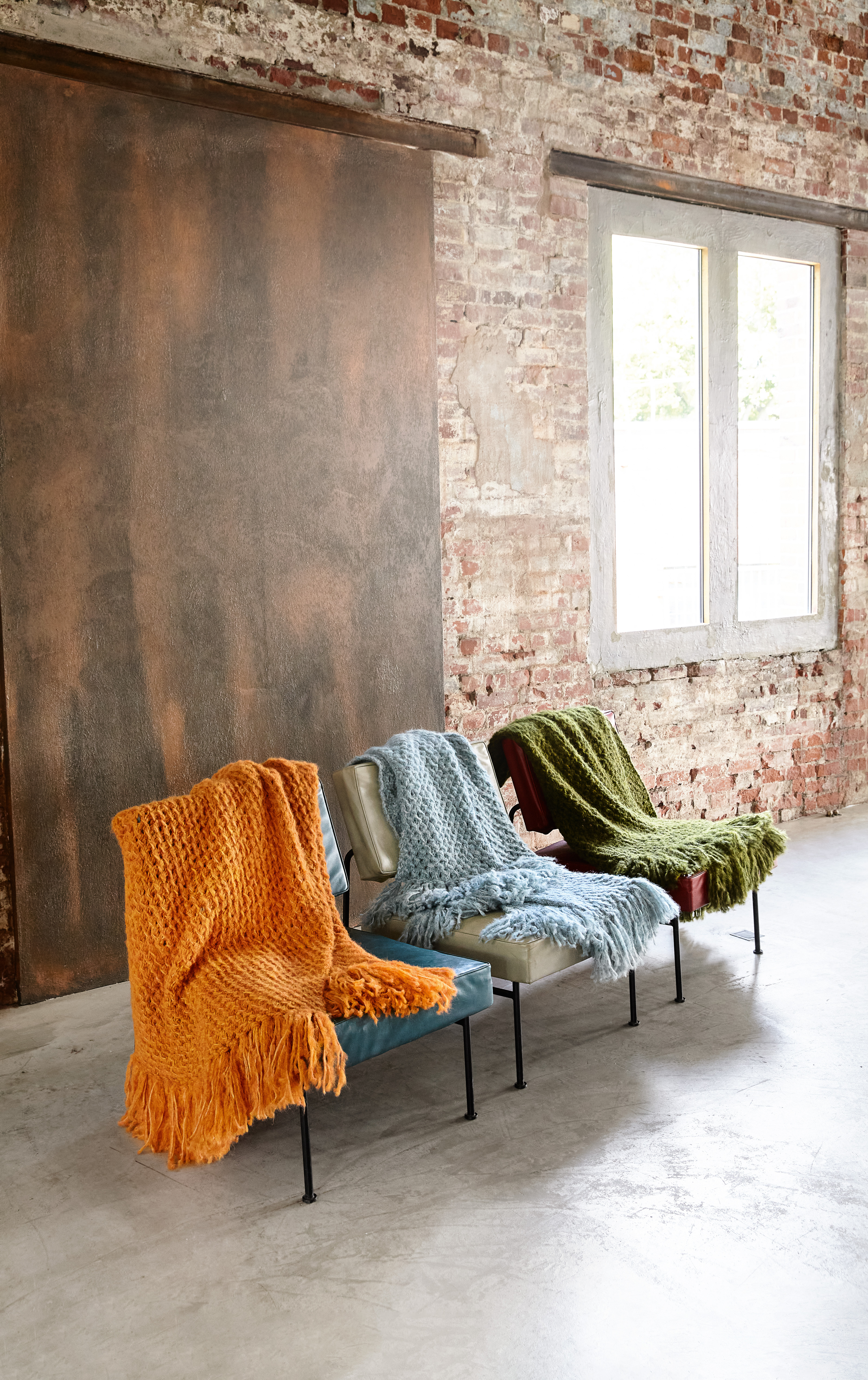 Handgestrickte Decken in Orange, Blau und Grün. Grobmaschig, weiche Textur, ideal für modernes Wohndesign.