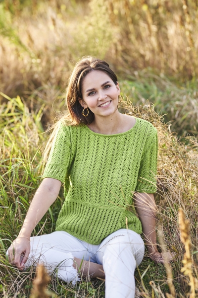 Modisches, handgemachtes, grünes Strickoberteil mit feinem Lochmuster, kombiniert mit schlichten weißen Hosen.