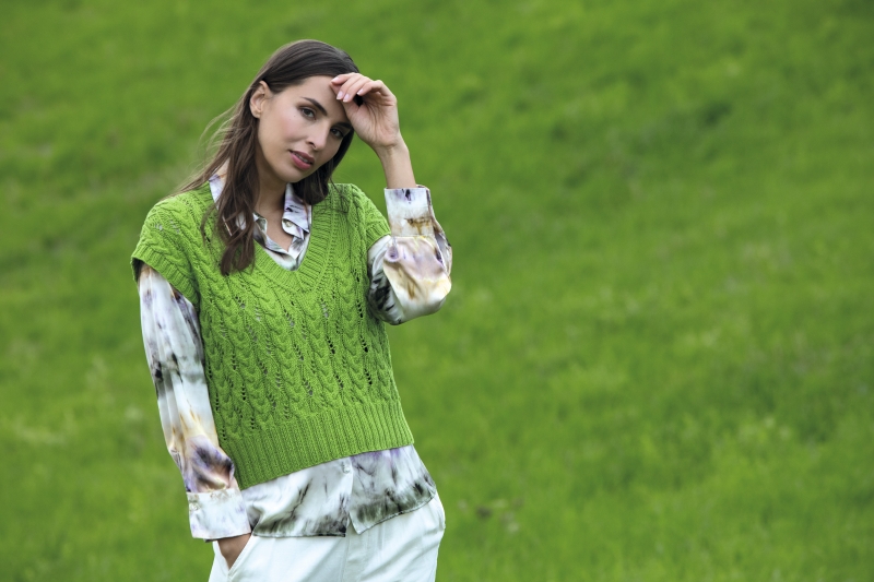 Grüner, gestrickter Pullover über einem gemusterten Hemd, kombiniert mit weißen Hosen. Stilvoll und handgemacht.