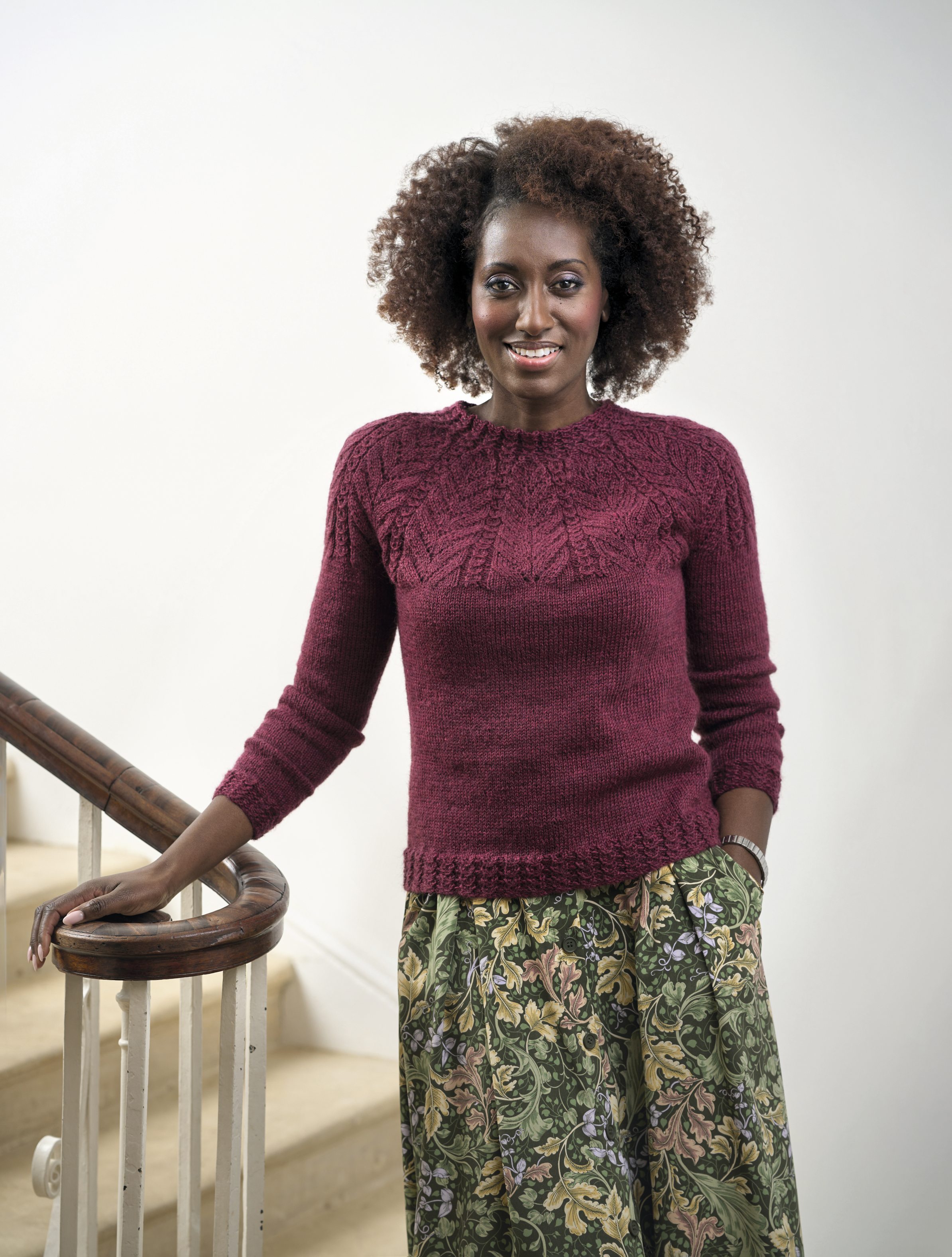 Handgestrickter bordeauxroter Pullover, strukturierter Kragen; floraler Maxirock, lebendig und kunstvoll.