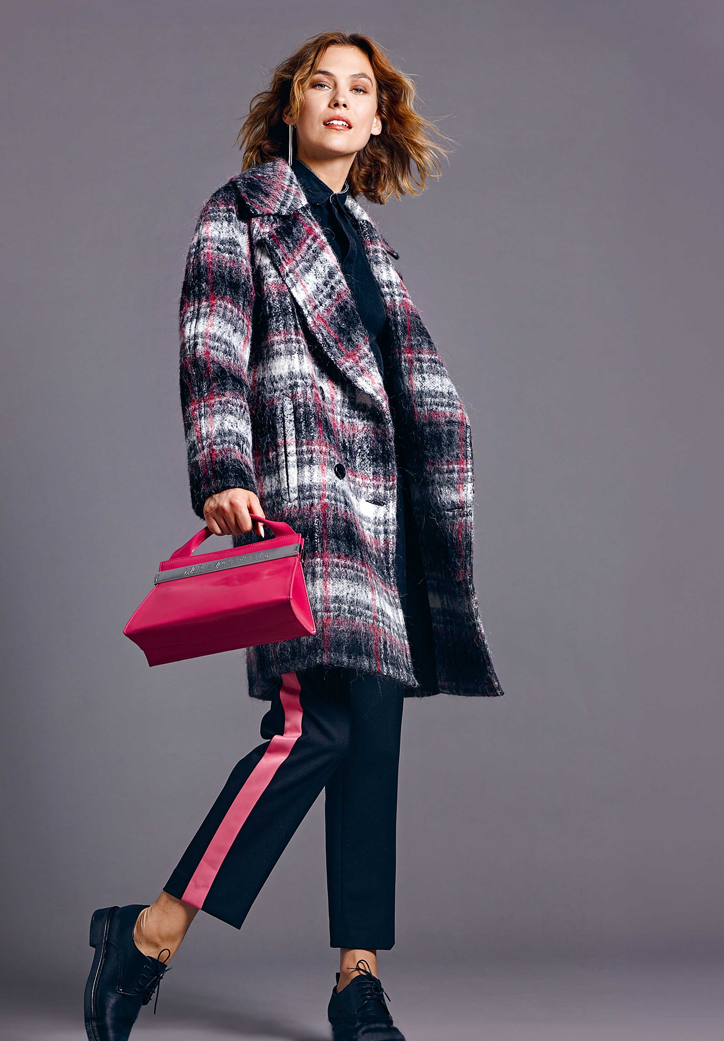 Modischer Mantel mit Karomuster, schwarzer Hose mit pinkem Streifen, pinke Handtasche. Trendy und chic.
