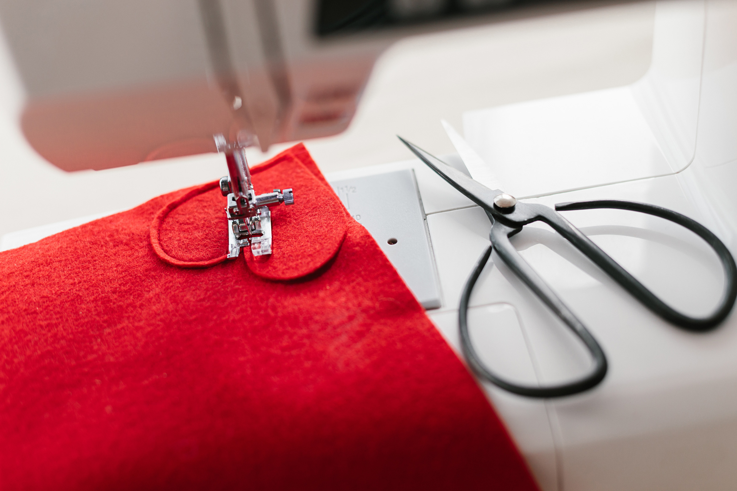 Leuchtend roter Stoff unter Nähmaschine; moderne, elegante Handarbeit, DIY-Look, Schere daneben.