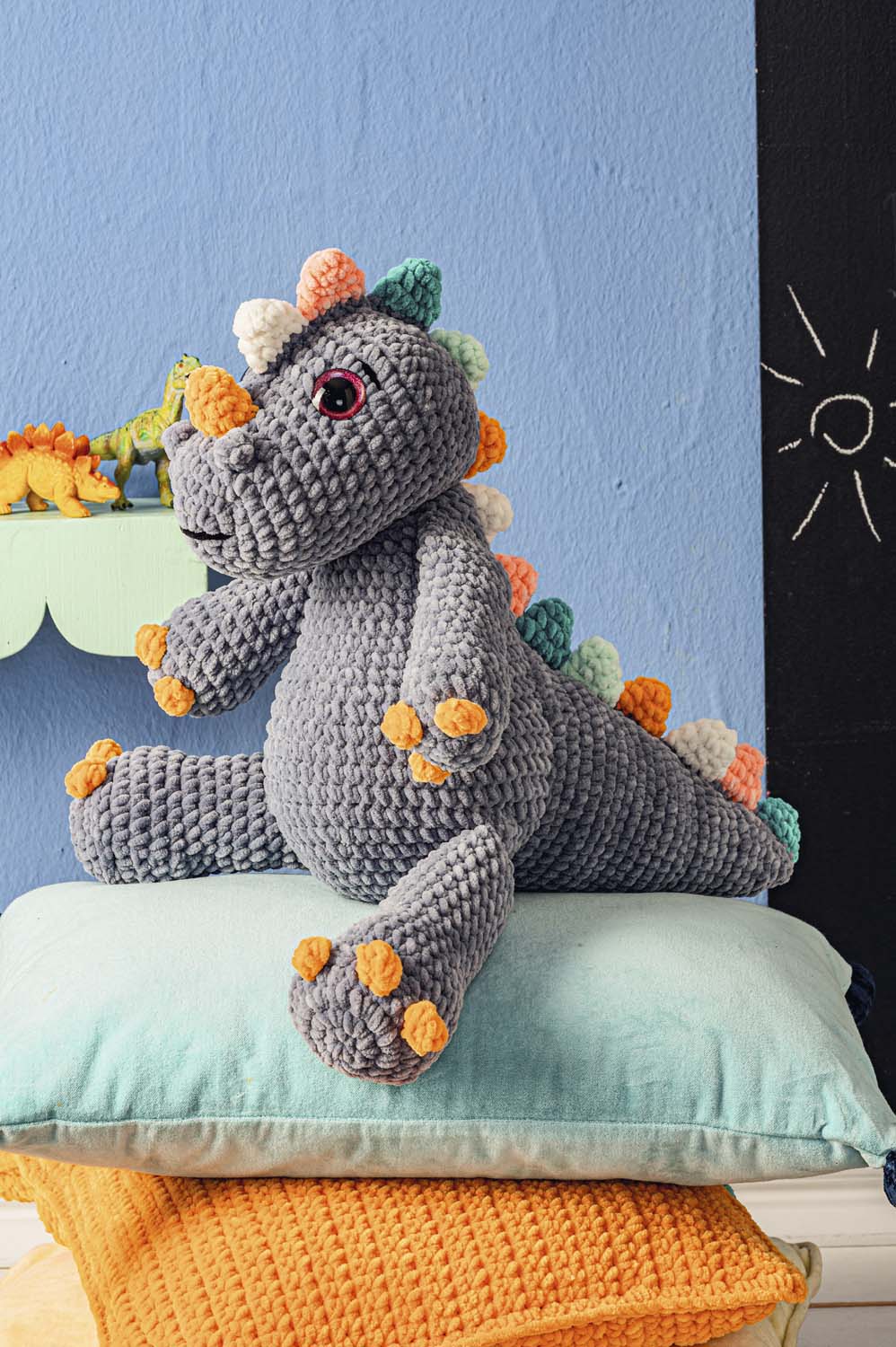 Grauer, gehäkelter Dinosaurier mit bunten Akzenten, handgemacht und liebevoll gestaltet.