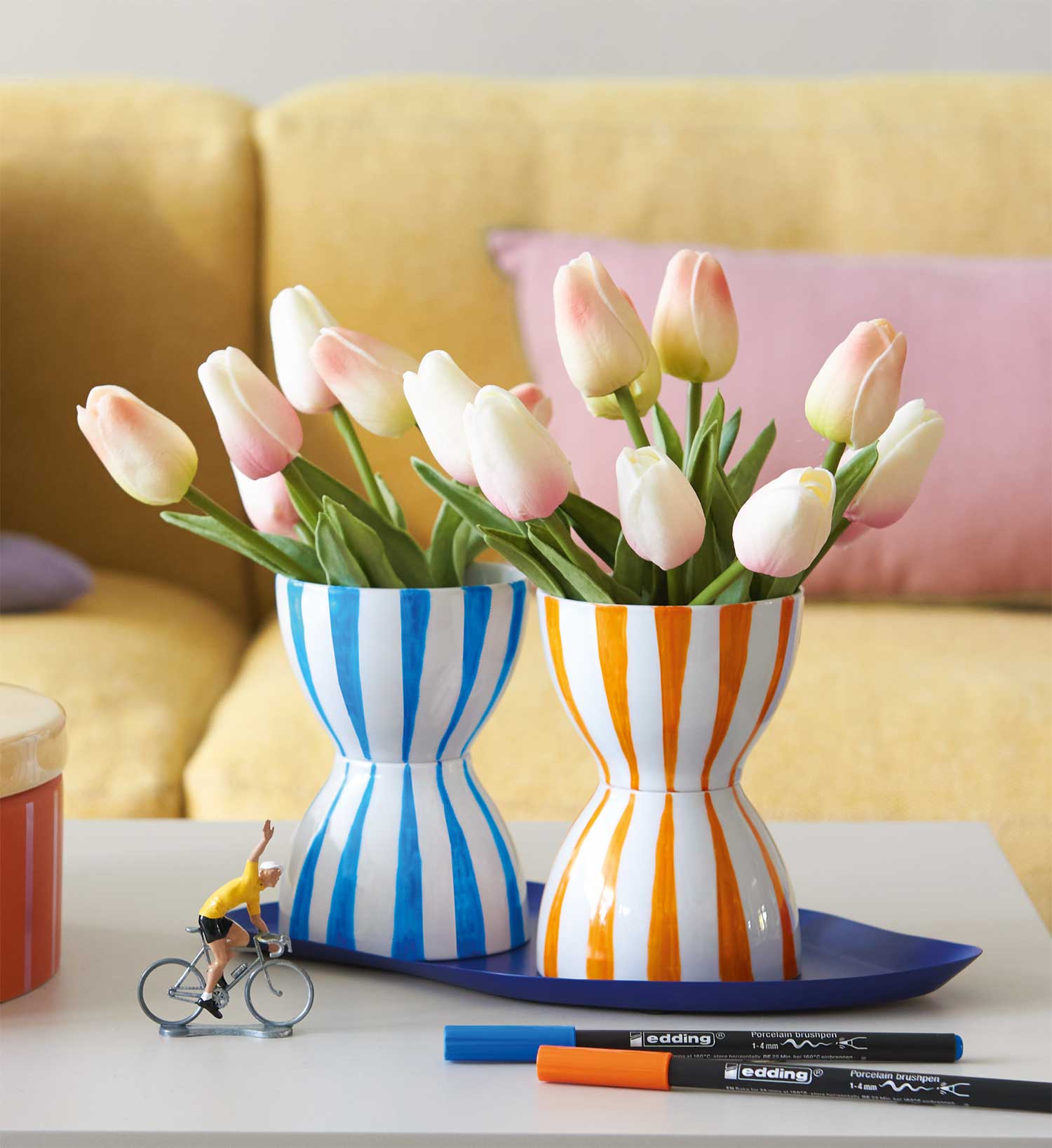 Zwei handbemalte Vasen mit blauen und orangefarbenen Streifen, gefüllt mit Tulpen. Modisch und selbstgemacht.