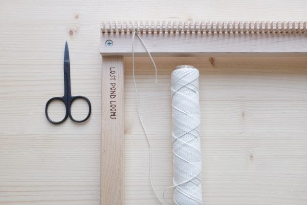 Minimalistischer, handgemachter Webrahmen aus Holz, begleitet von Schere und Garnrolle. Bastelspaß!