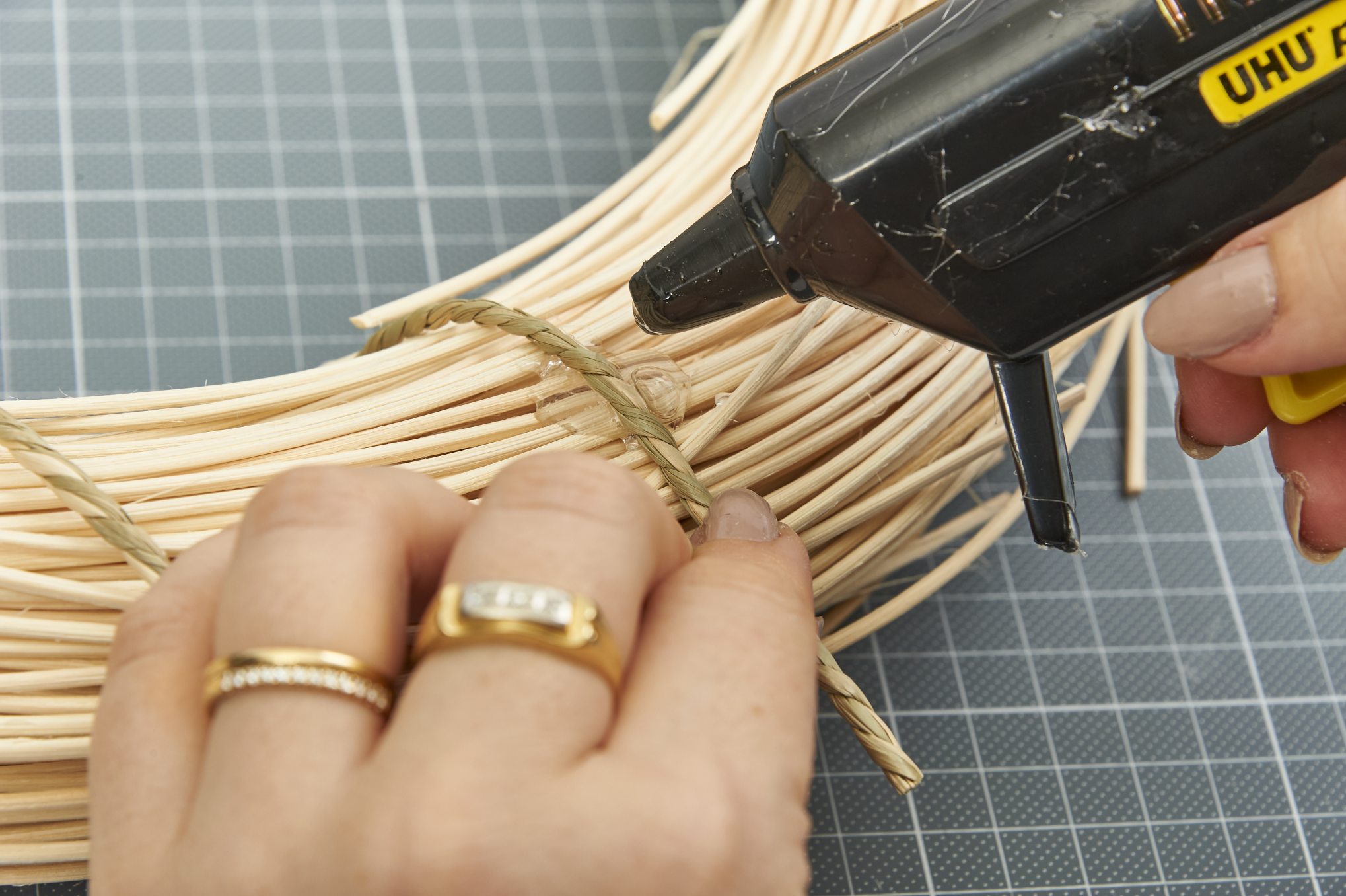 Handwerkliche Kranzgestaltung mit Naturmaterialien, heiße Klebepistole und goldene Accessoires. Kreative Bastelarbeit.