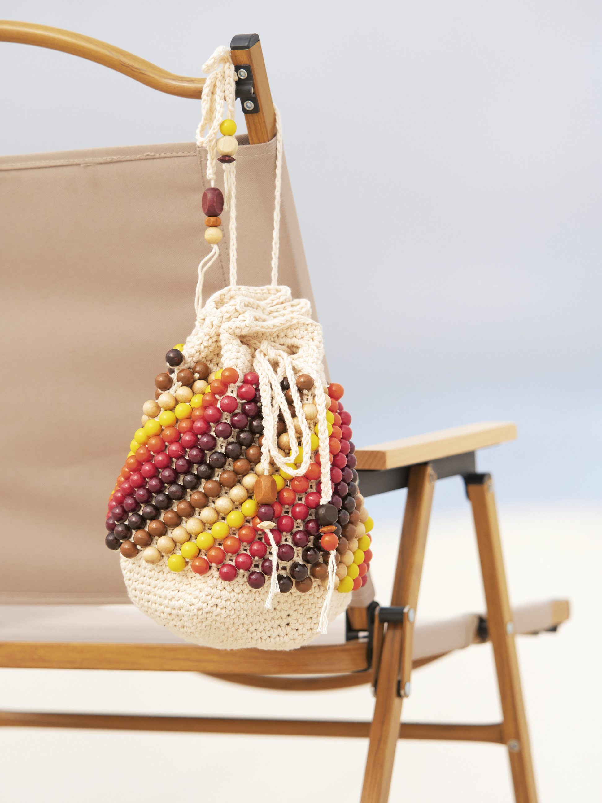 Handgemachte Tasche mit bunten Holzperlen, cremefarbenes Gehäkel, DIY-Look, boho-inspirierter Stil.