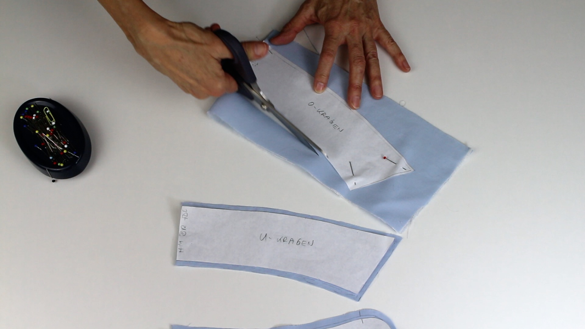 Hellblauer Stoff, Schnittmuster aufgesteckt. Schere und Stecknadeln für DIY und modisches Nähen.