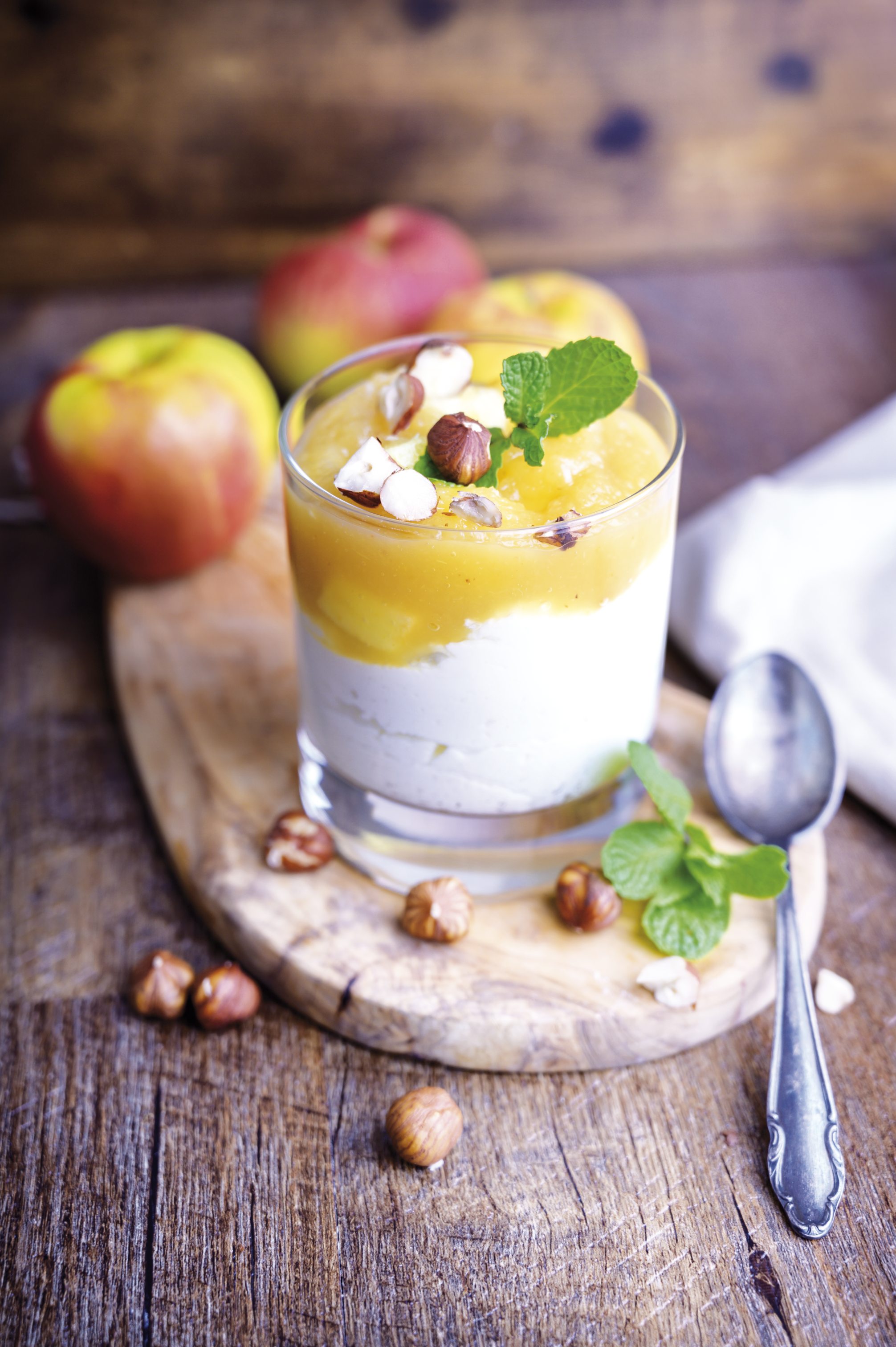 Schichtdessert mit Sahne und Fruchtpüree, garniert mit Minzblatt und Haselnüssen, rustikal serviert.