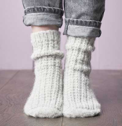 Weiße, handgearbeitete Stricksocken mit Zopfmuster, modischer Look, ideal für gemütliche Tage.