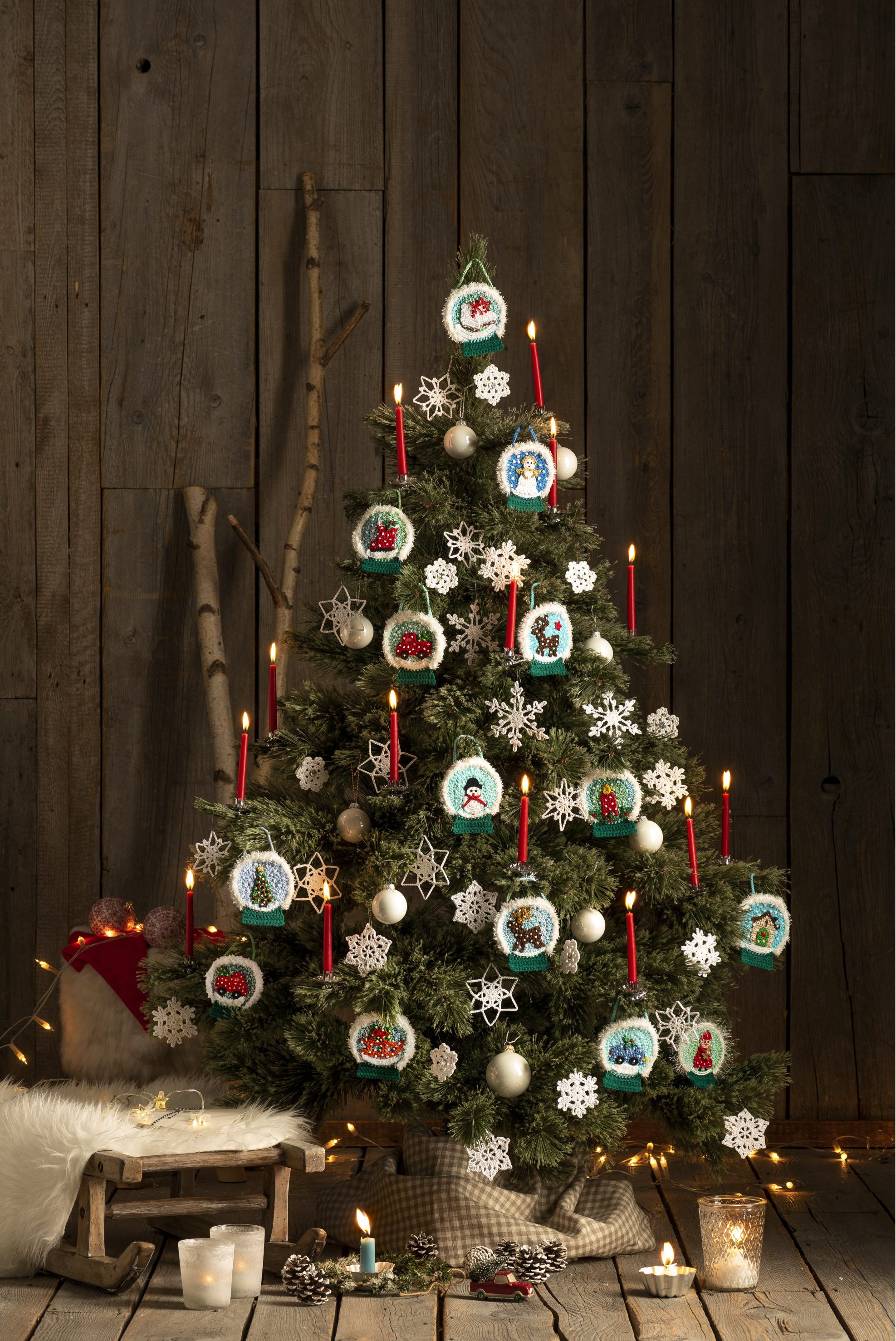 Selbstgemachtes Baumdekor mit gestrickten Kugeln, weißen Schneeflocken und roten Kerzen. DIY, festlich, kreativ.