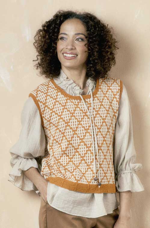Orange-weiße, handgemachte Häkelweste über beige Bluse. Zeitloses Muster mit DIY-Charme.