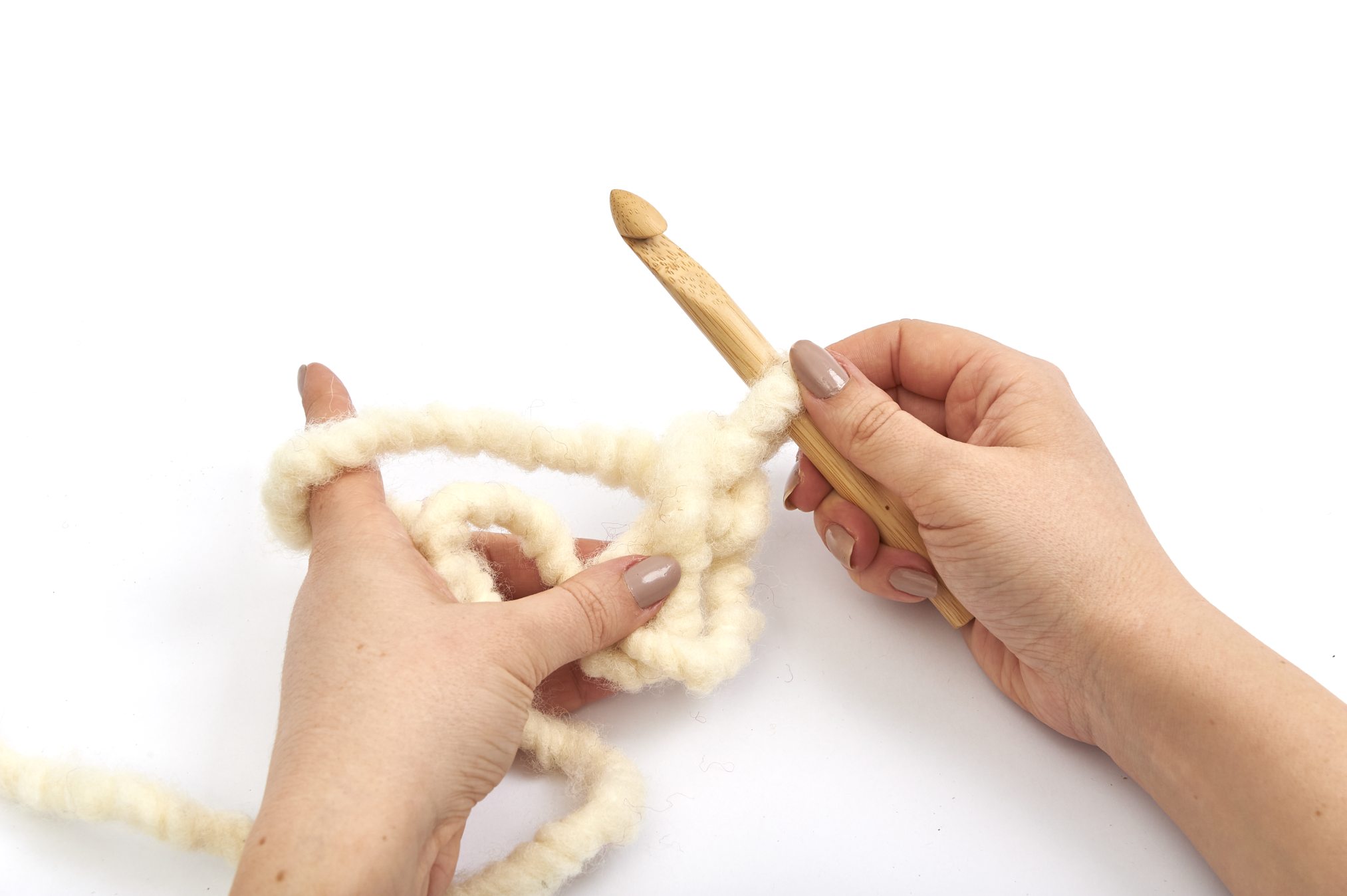 Grobe, cremefarbene Wolle wird mit Holzhäkelnadel verarbeitet. DIY, selbstgemacht, modisch.