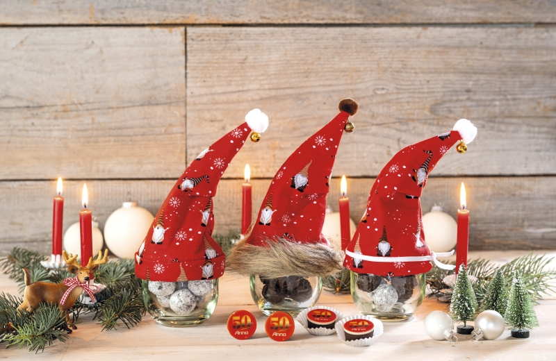 Rote, handgemachte Mützen mit Schneeflöckchen- und Pinguin-Muster auf Gläsern. Modische, festliche Handarbeit.
