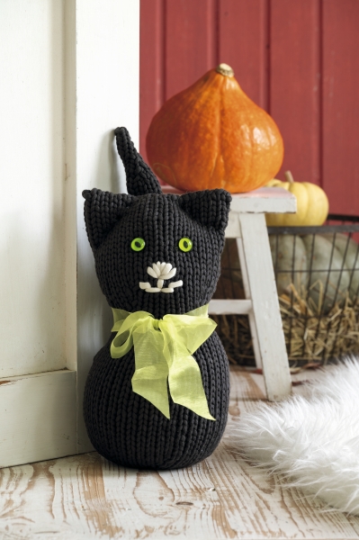 Handgemachte schwarze Katze, gestrickt, mit grüner Schleife und Knopfdetails. Modisches DIY-Projekt.