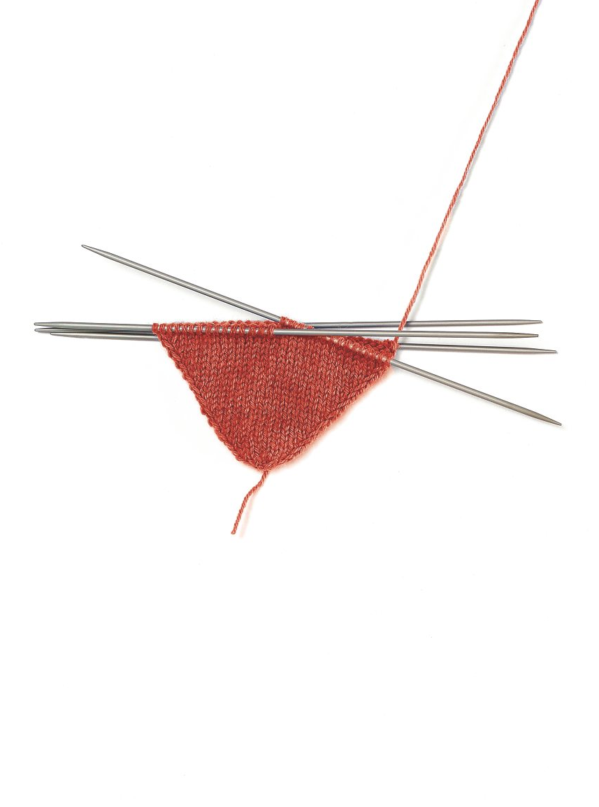 Handgemachte, dreieckige Strickarbeit in Rot, mit feinen Nadeln, glattes Muster, selbstgemachte Eleganz.