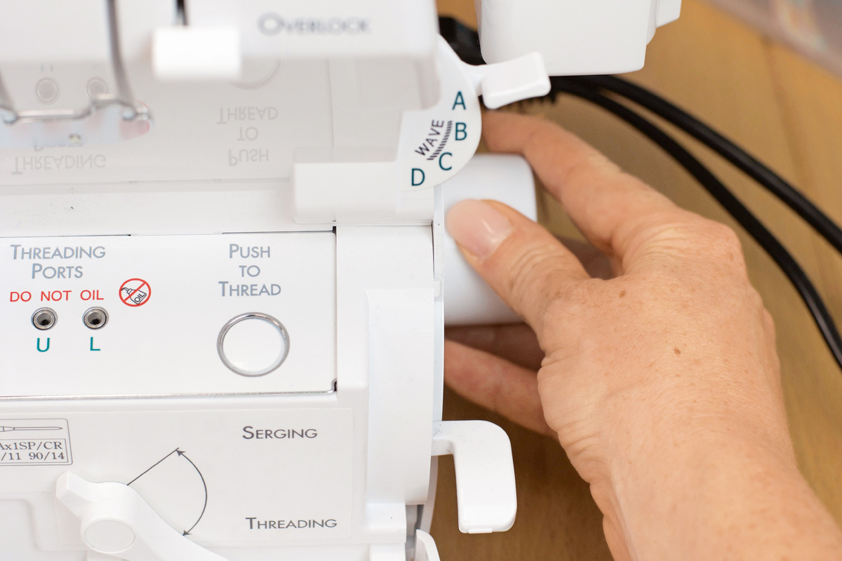 Nahaufnahme: Hand bedient weiße Overlock-Nähmaschine, detailreiche Knöpfe, ideal für DIY-Mode.