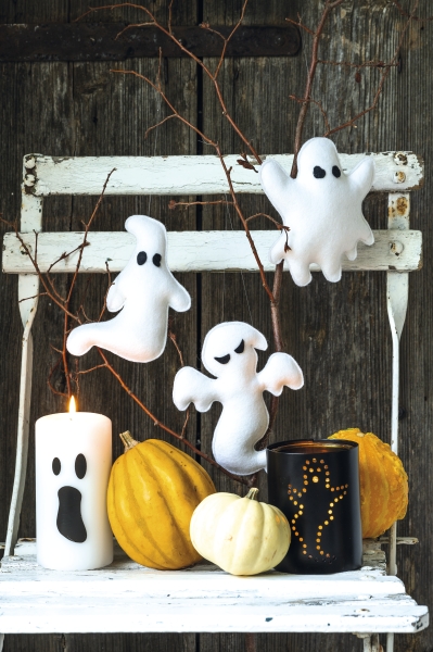 Handgemachte weiße Geister aus Stoff, ergänzt durch modische, geschnitzte Kerzen und dekorative Kürbisse.