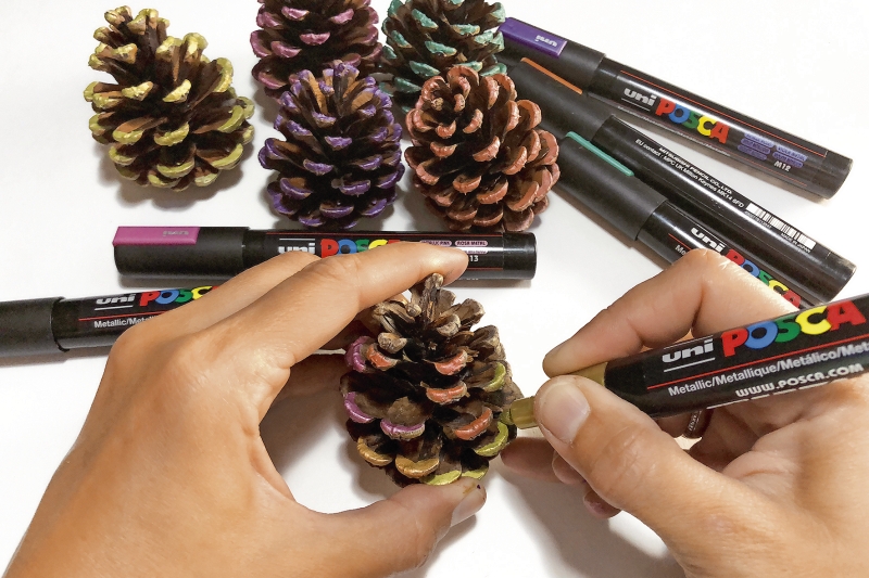Metallisch bemalte Zapfen mit DIY-Charakter. Lebendige Farben und kreatives Handwerk.