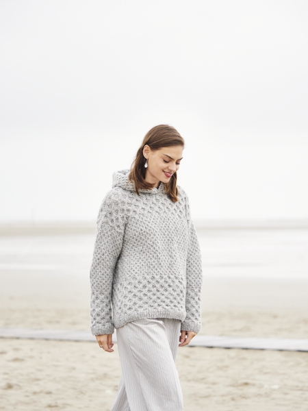 Grob gestrickter, grauer Pullover mit Zopfmuster. Weit, selbstgemacht. Beige Hose, lässig. Modisch, handgemacht.