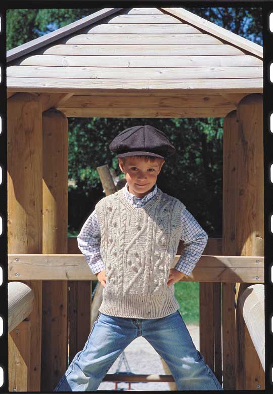 Strickweste mit Zopfmuster, modisch; Cordkappe, rustikal; helle Jeans, lässig.