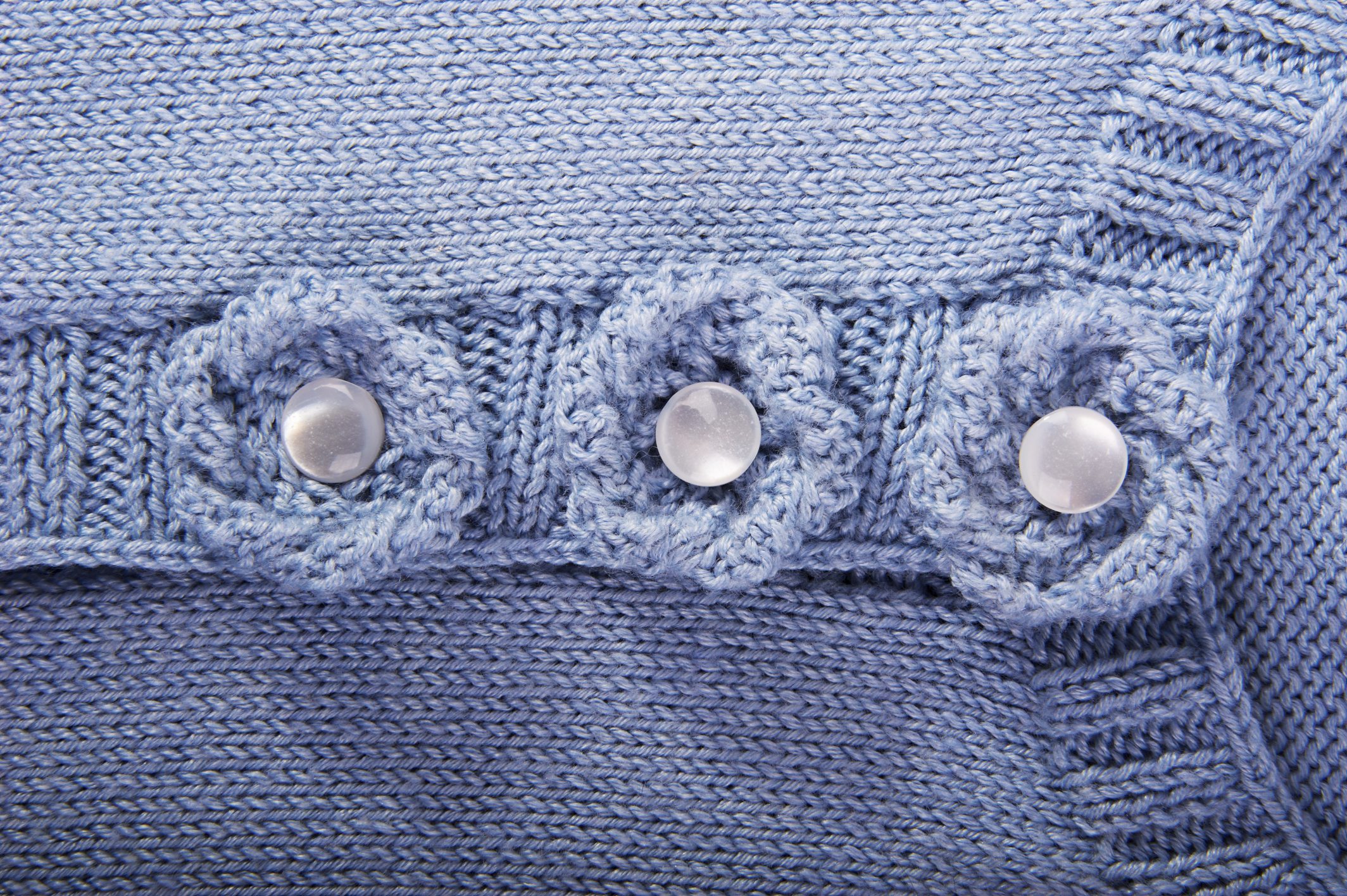 Handgefertigter blauer Strickstoff mit Blumenmuster und runden Knöpfen. Modisch, kunstvoll, diy.