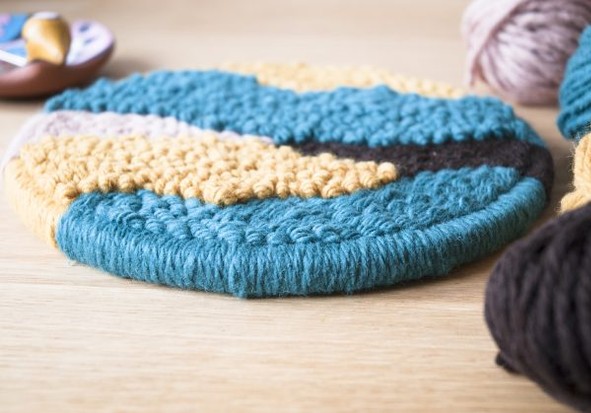 Runder Untersetzer, gehäkelt aus blauem, beigem und braunem Garn. DIY-Chic, einzigartiges Muster.