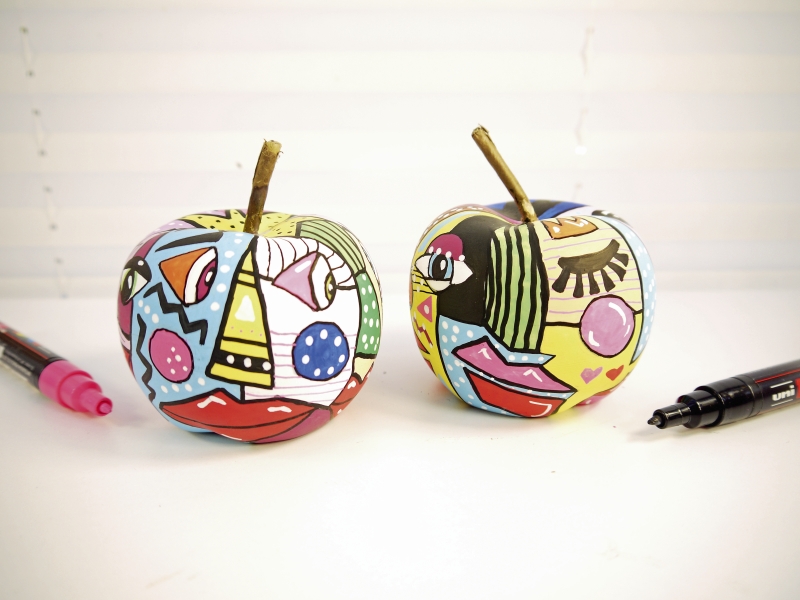 Zwei Äpfel im modisch bunt gemusterten DIY-Stil, mit grafischen Elementen und leuchtenden Farben bemalt.