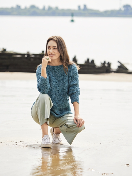 Modischer blauer Strickpullover, handgemacht, kombiniert mit weiten, hellen Hosen. Lässig mit Sneakern.