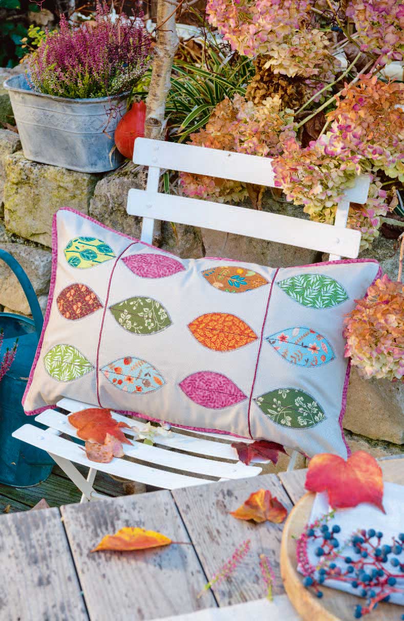 Handgemachtes Kissen mit bunten Blättermotiven, herbstlich, lebendige Farben, kunstvolles Patchwork-Design.