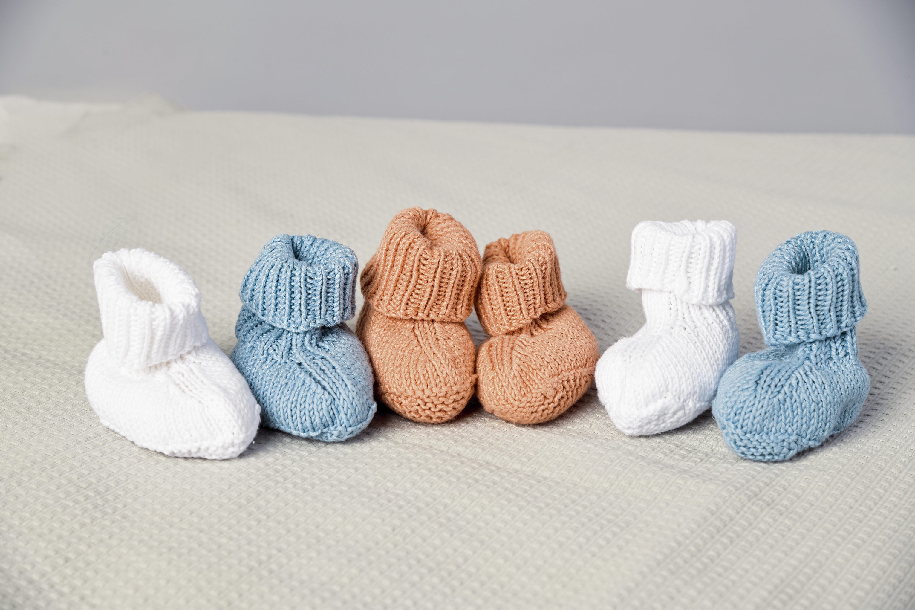 Niedliche, handgefertigte Babyschuhe in Blau, Weiß und Braun. Weiches Strickmuster, ideal für sanfte Babyfüße.