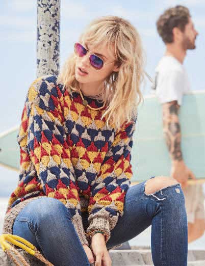 Modisch gemusterter Pullover in kräftigen Farben, kombiniert mit zerrissenen Jeans. Handarbeit-Chic.