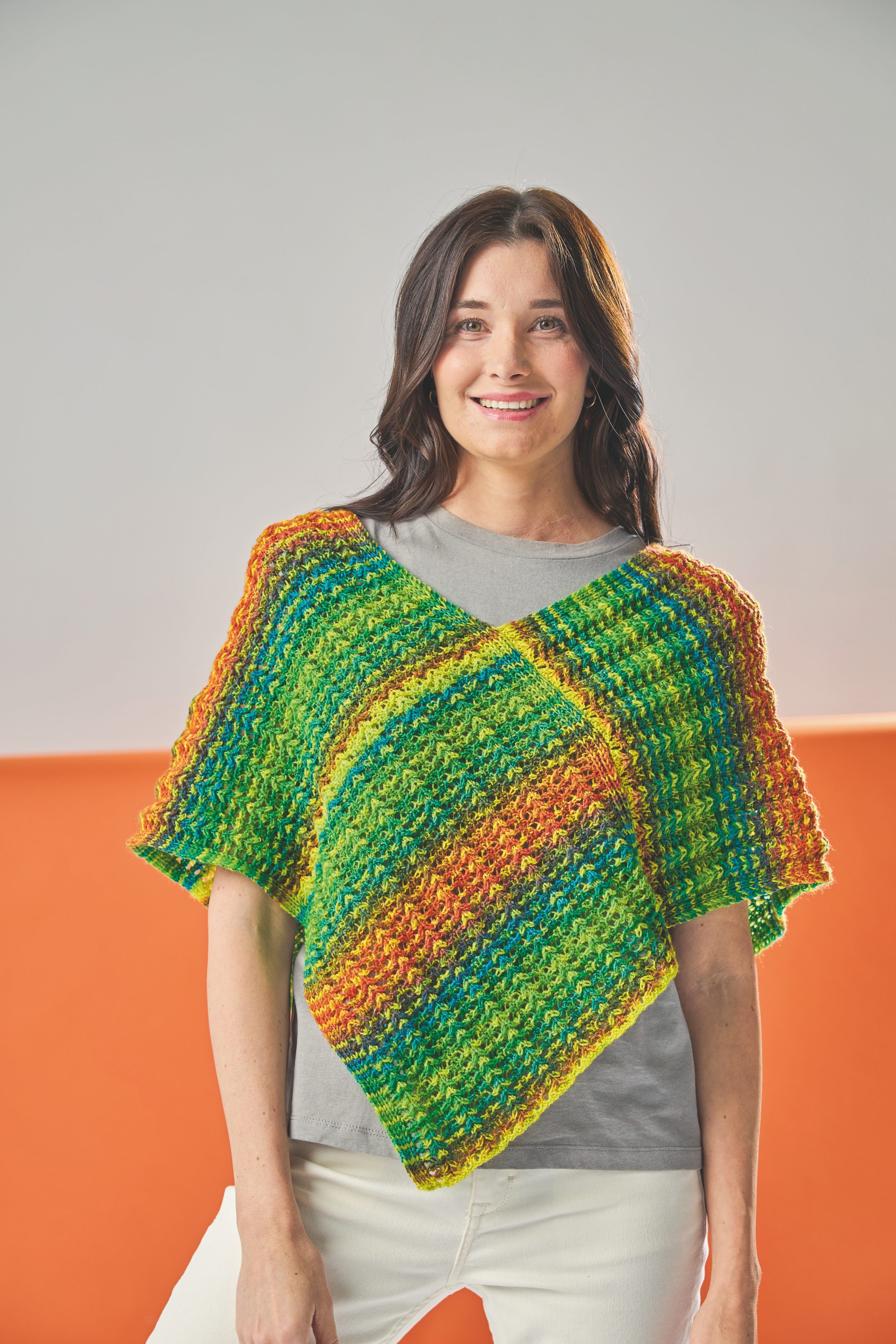 Farbenfroher handgemachter Poncho in Regenbogenmuster; kurz und modisch mit strukturierter Textur.