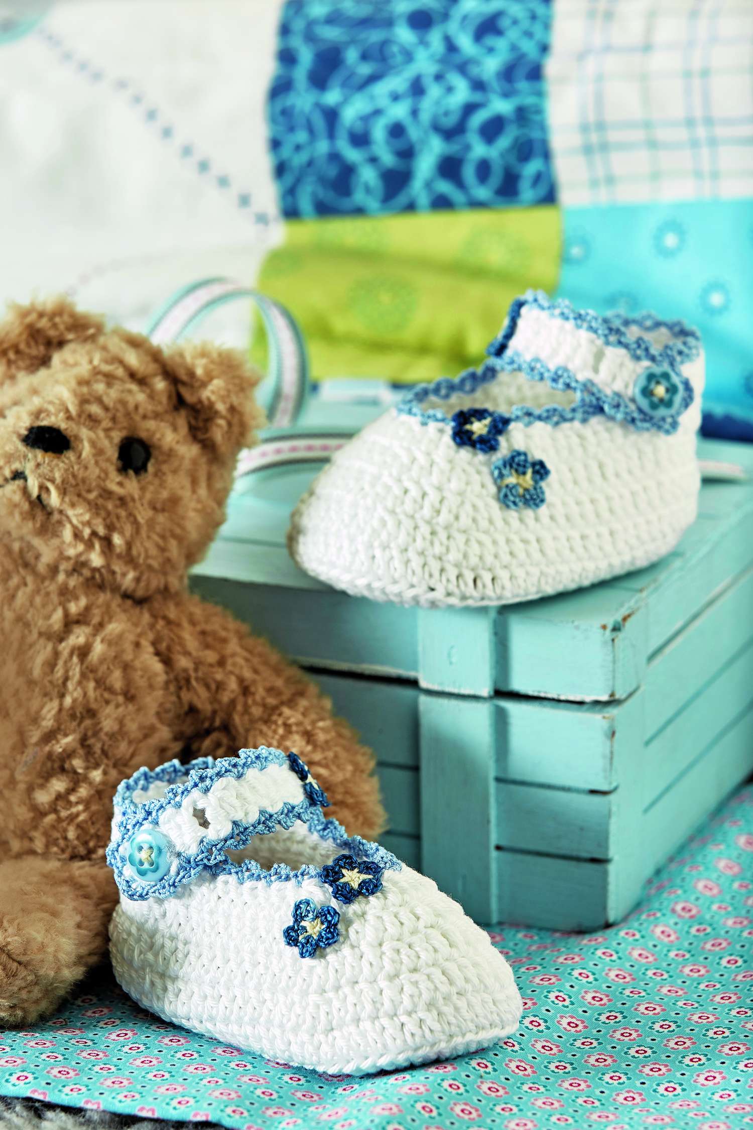 Weiße, handgemachte Babyschuhe mit blauen Blumen und Spitzenrand. Modisch, zart, detailreich.