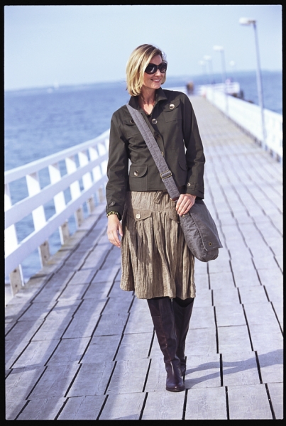 Beige Faltenrock, dunkelgrüne Jacke, kniehohe Stiefel. Modisch und casual, ideal für kühle Tage.