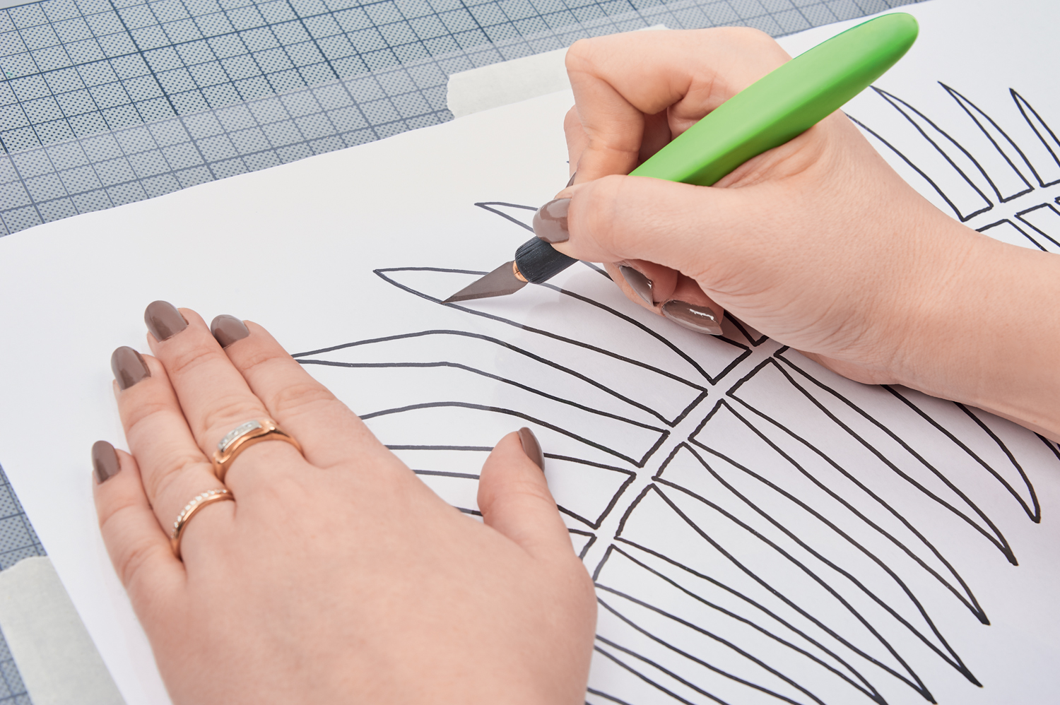 Hand schneidet Blattmuster aus Papier. DIY, handgemacht, künstlerisch, schwarz-weiß, präzise Linien, kreativer Prozess.