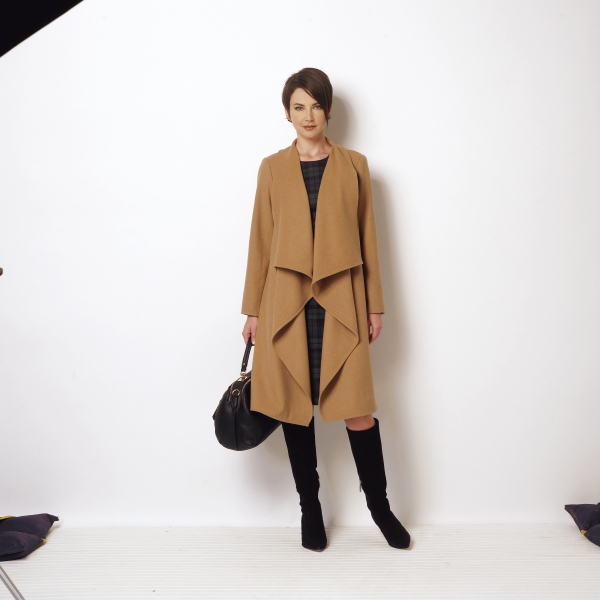 Kamelmantel mit Wasserfall-Design, kombiniert mit schwarzem Kleid, hoher Stiefel und Tasche. Zeitlos und stilvoll.