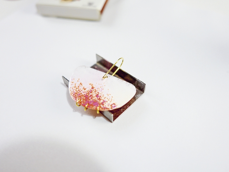 Modisch geschwungener Ohrring in Weiß mit rosa-goldenen Akzenten, handgefertigt aus selbstgemachten Materialien.