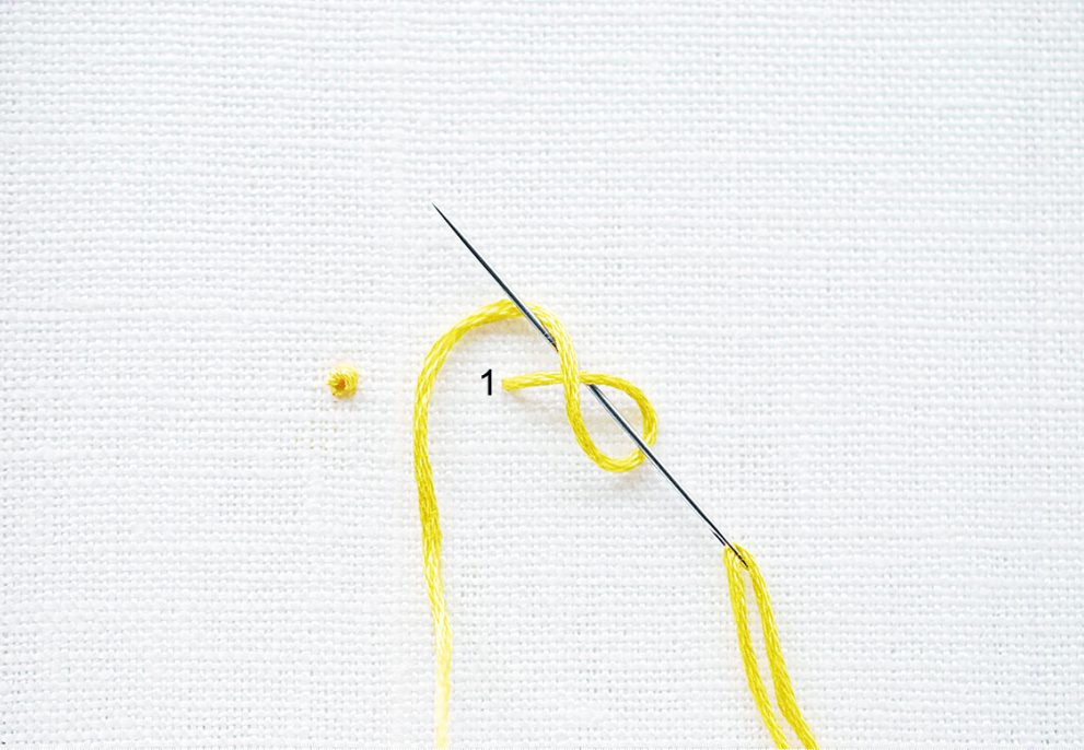 Gelber Faden im handgemachten Stickmuster auf weißem Stoff. DIY-Kreativität.
