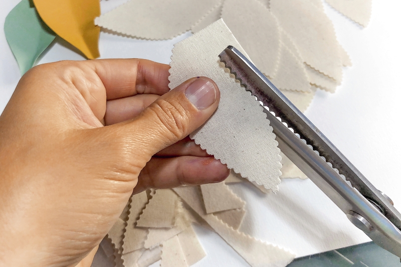 Gezackte Schere schneidet beige Stoffblätter. DIY, handgemacht, kreativ.