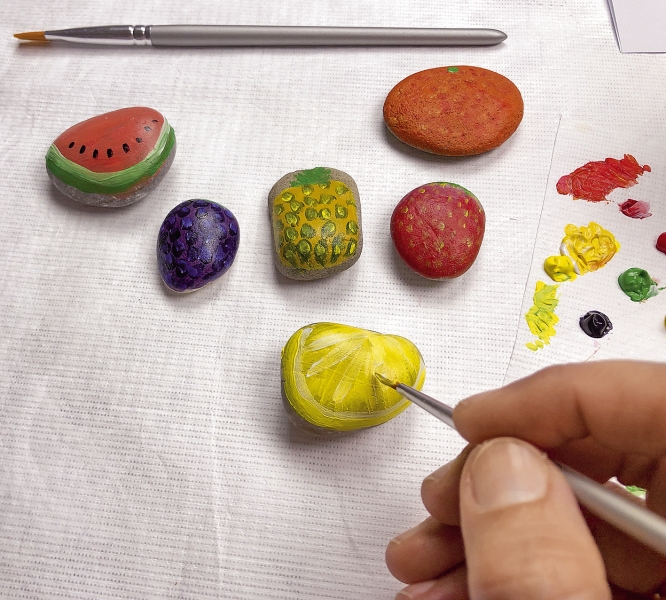 Bunte, handbemalte Steine in Fruchtform; DIY-Kunst mit kräftigen Farben und detailreichen Mustern.