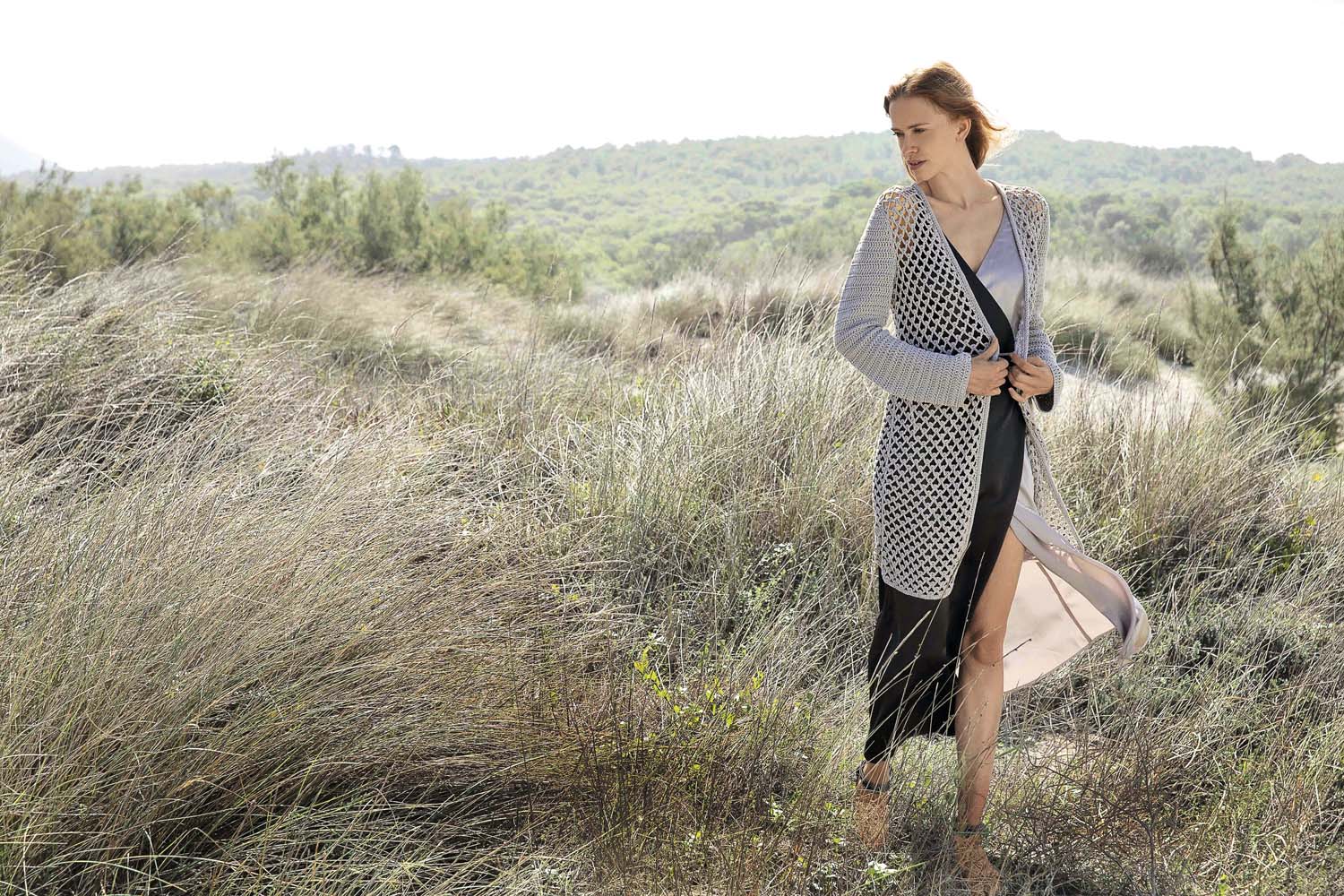 Grauer, handgemachter Mantel mit grobem Mesh-Muster, modisch und stilvoll über einem schwarzen Kleid getragen.