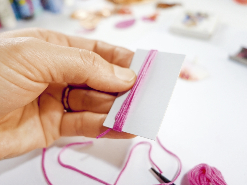 Hand wickelt rosa Faden um Papier; DIY, handgemacht, kreative Handarbeit.