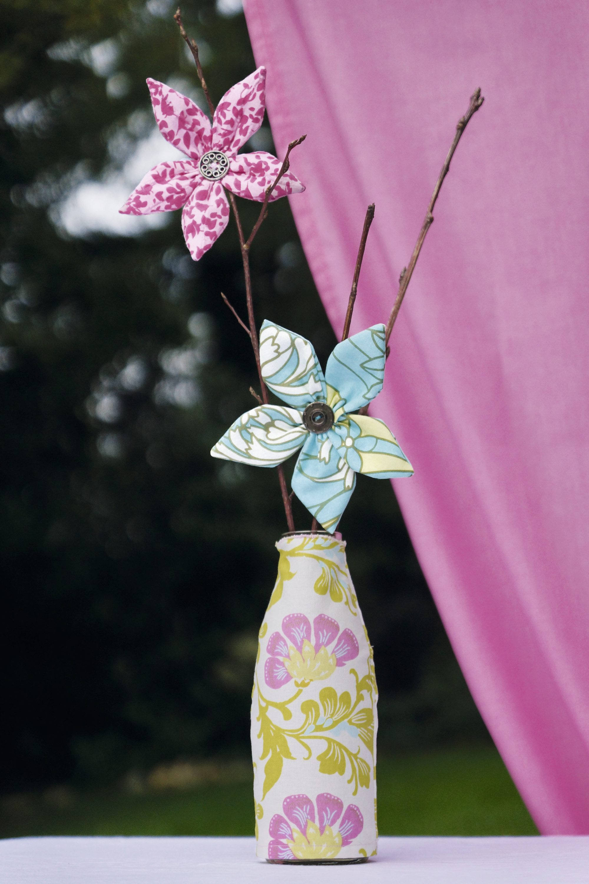 Zarte DIY-Stoffblumen in Rosa und Türkis mit Knopf, in gemusterter Vase, romantisch und handgemacht.