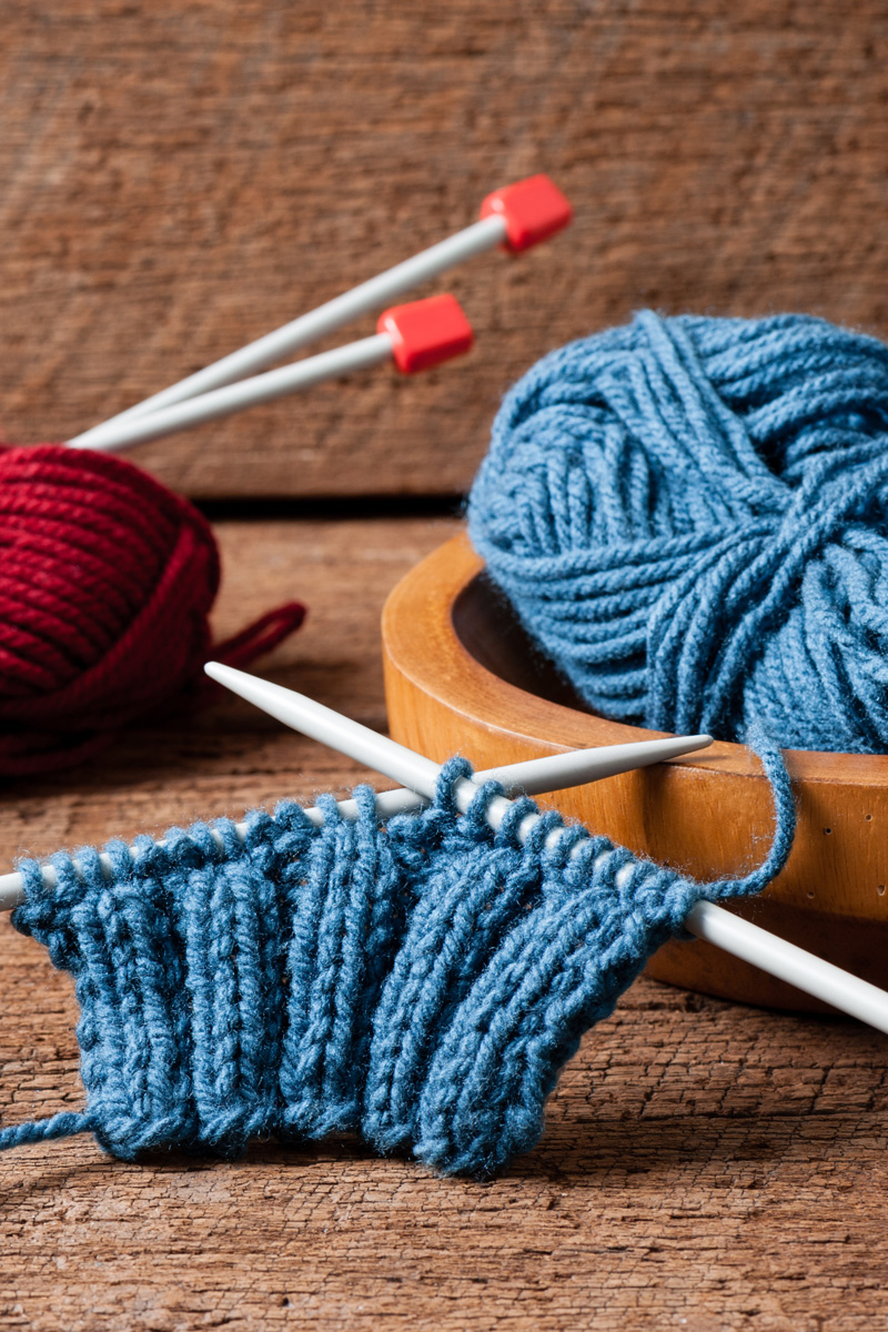 Blaue und rote Wolle, Stricknadeln; handgemachtes Strickprojekt; modisch, kreativ.