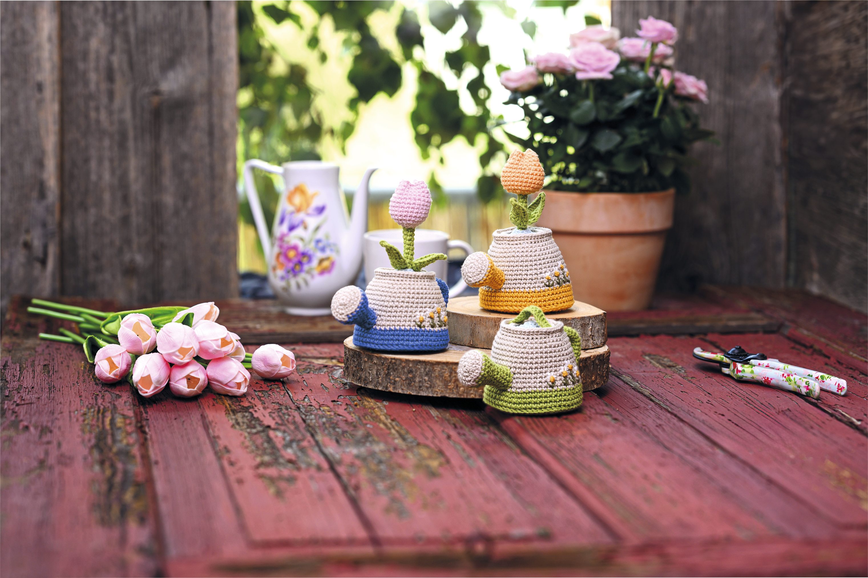 Farbenfrohe, gehäkelte Gießkannen mit Blumendesign. DIY-Look, modisch und detailreich gestaltet.