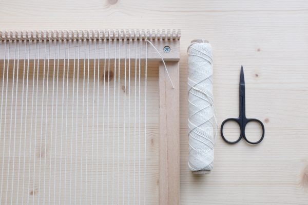 Hellbeiger Faden und Schere neben Webrahmen. Kreativ, handgemacht, Handarbeit.